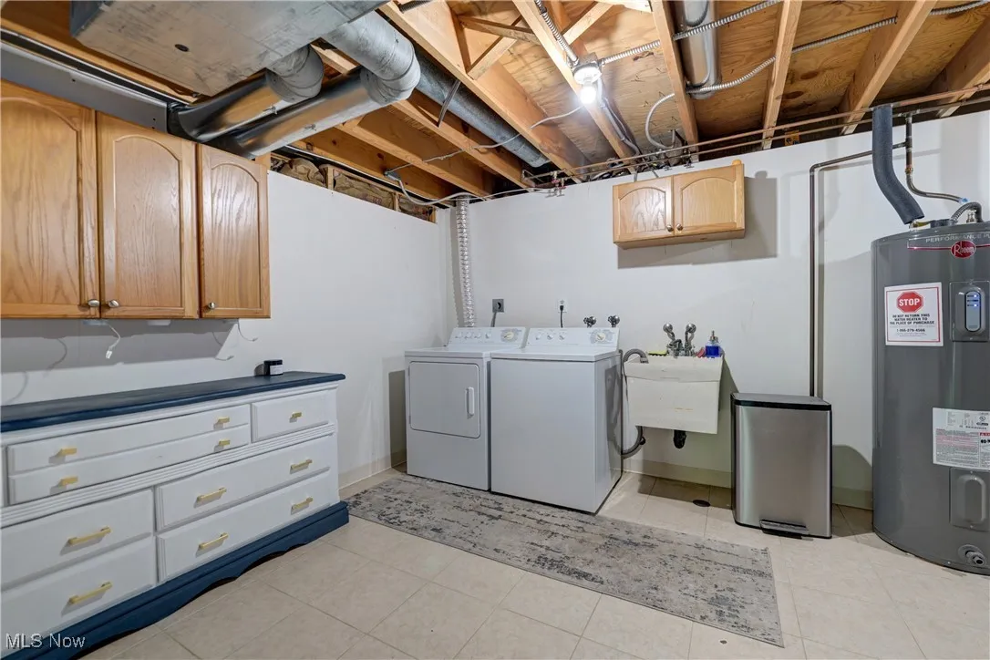 Laundry area with cabinet space, water heater, light tile patterned floors, and separate washer and dryer