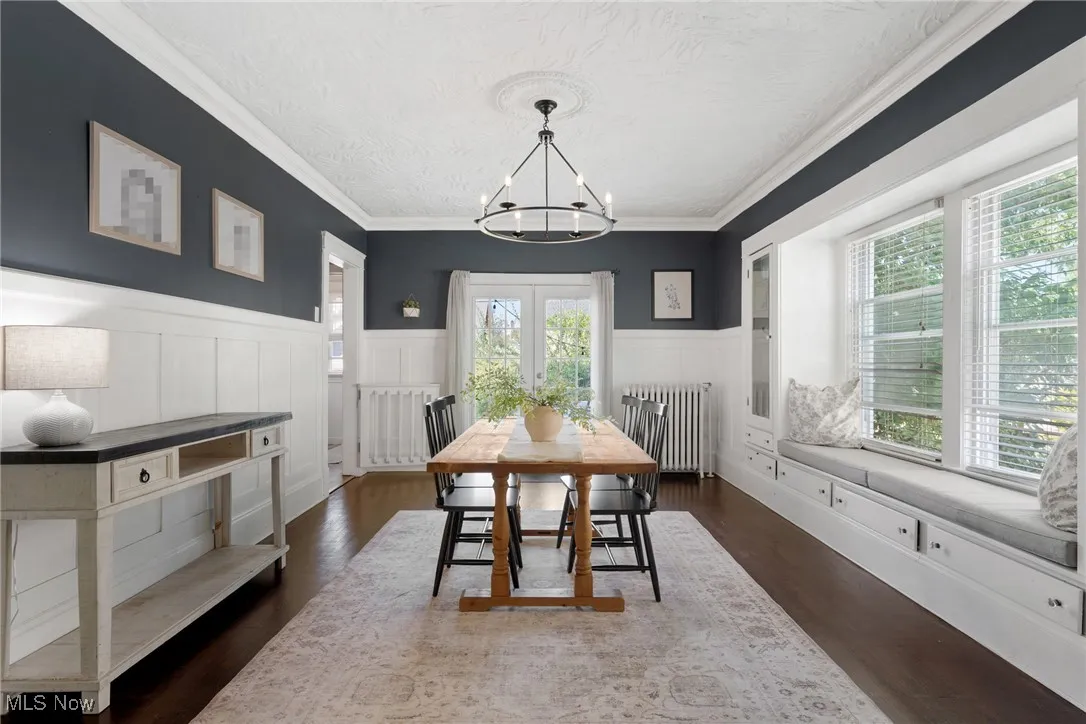 Dining room featuring radiator, dark wood-style floors, a wainscoted wall, a chandelier, and ornamental molding