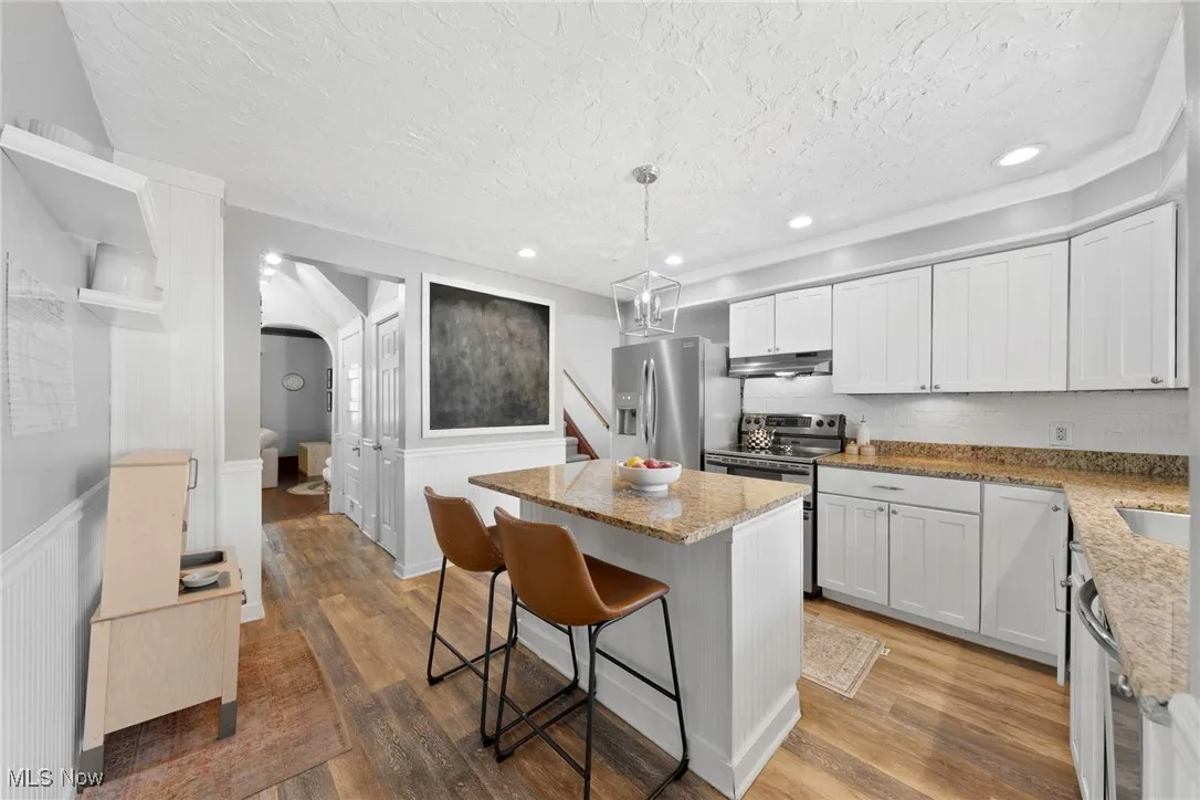 Kitchen with a kitchen bar, white cabinetry, light stone counters, a center island, and a wainscoted wall