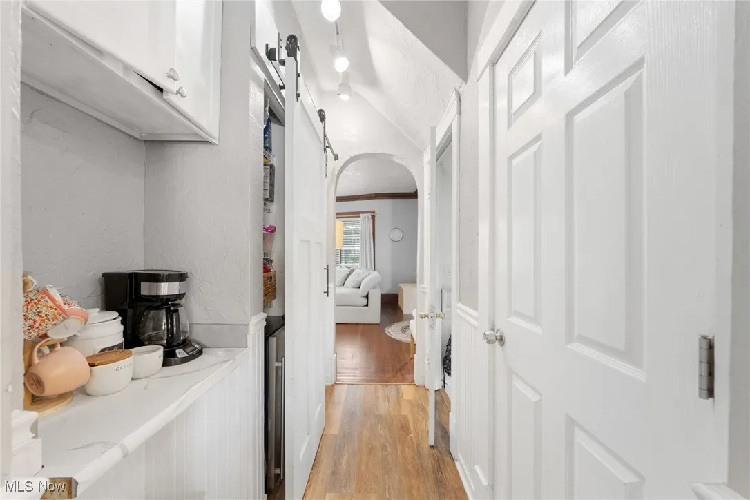 Hallway with a barn door, arched walkways, light wood-type flooring, a textured wall, and ornamental molding