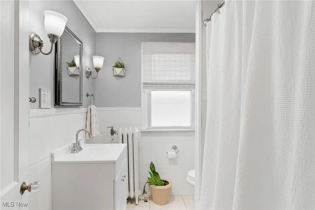 Bathroom featuring vanity, crown molding, radiator heating unit, wainscoting, and light tile patterned floors