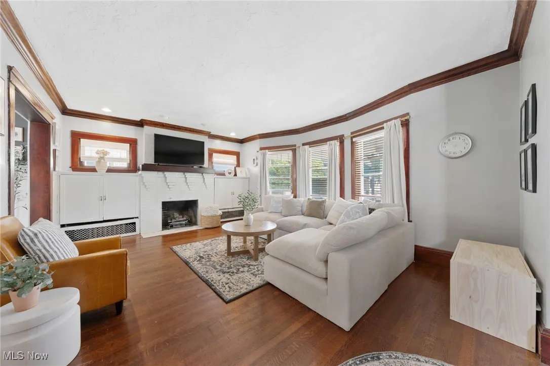 Living room with dark wood-type flooring, a brick fireplace, and ornamental molding