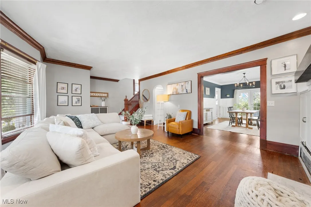 Living room with dark wood-type flooring, ornamental molding, stairway, and a chandelier