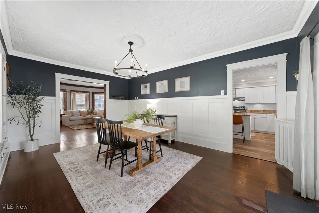 Dining room featuring a textured ceiling, a decorative wall, a wainscoted wall, crown molding, and dark wood-type flooring