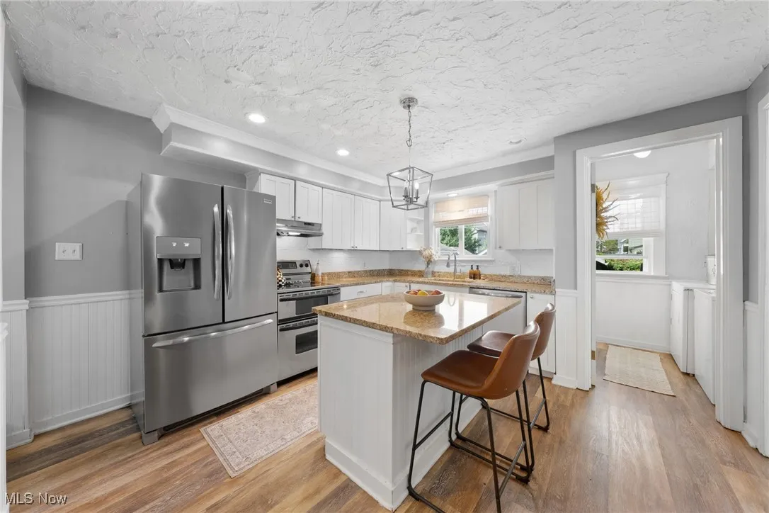 Kitchen featuring wainscoting, stainless steel appliances, light stone countertops, a breakfast bar area, and white cabinetry