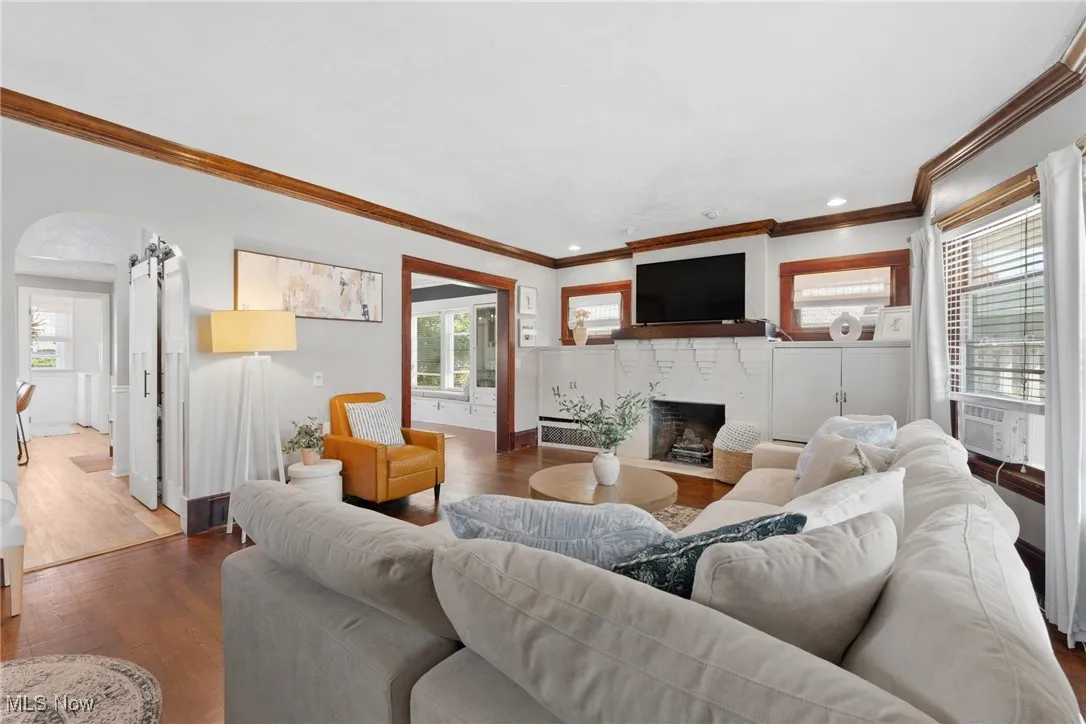 Living room with a brick fireplace, ornamental molding, wood finished floors, recessed lighting, and arched walkways