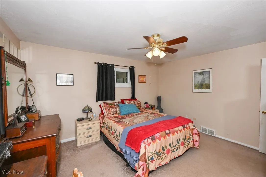 Primary bedroom with ceiling fan and carpet.