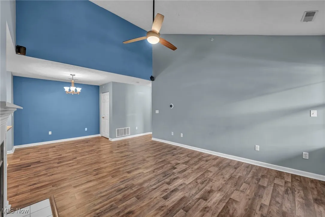 Unfurnished living room with high vaulted ceiling, wood finished floors, a fireplace, a chandelier, and a ceiling fan