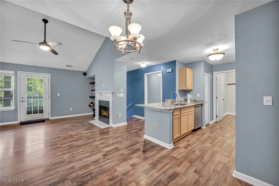 Kitchen featuring open floor plan, a chandelier, a fireplace with flush hearth, lofted ceiling, and a peninsula