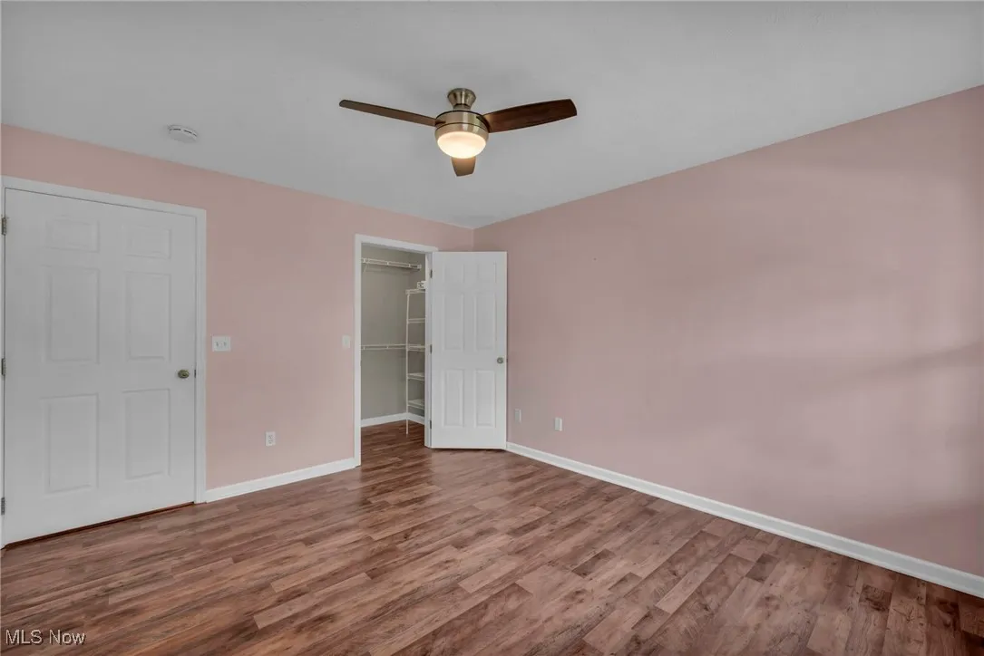 Unfurnished bedroom with wood finished floors, a spacious closet, and a ceiling fan