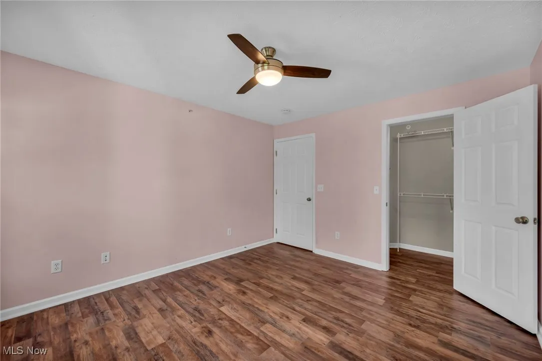 Unfurnished bedroom featuring a spacious closet, dark wood finished floors, and a ceiling fan