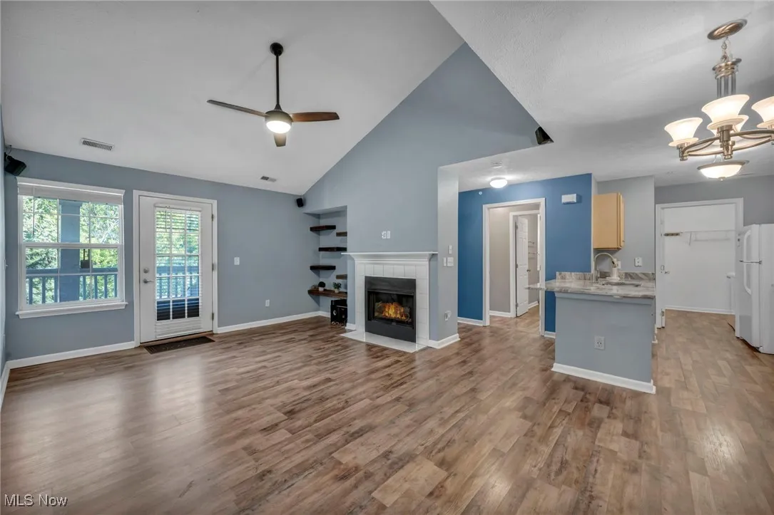 Unfurnished living room featuring ceiling fan, a tile fireplace, wood finished floors, high vaulted ceiling, and a chandelier