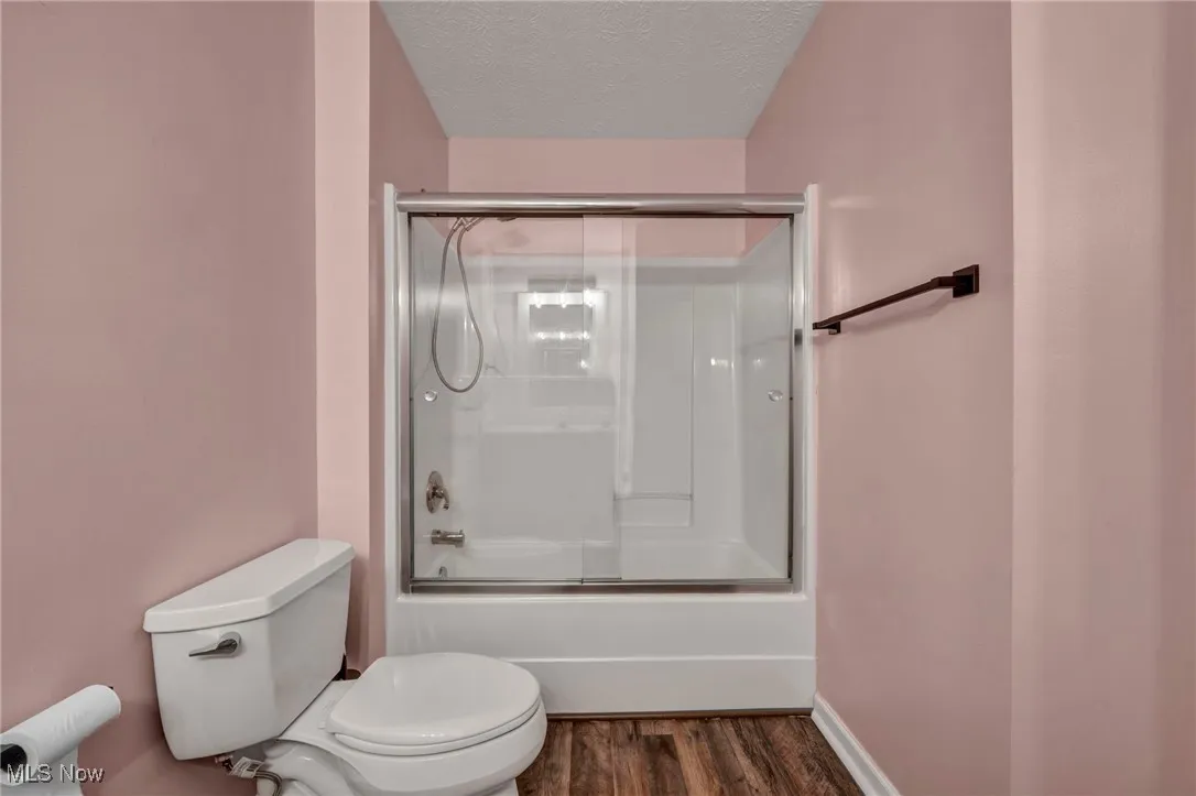 Bathroom featuring enclosed tub / shower combo, a textured ceiling, and dark wood-type flooring