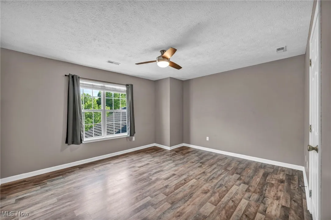 Spare room with wood finished floors, a textured ceiling, and a ceiling fan