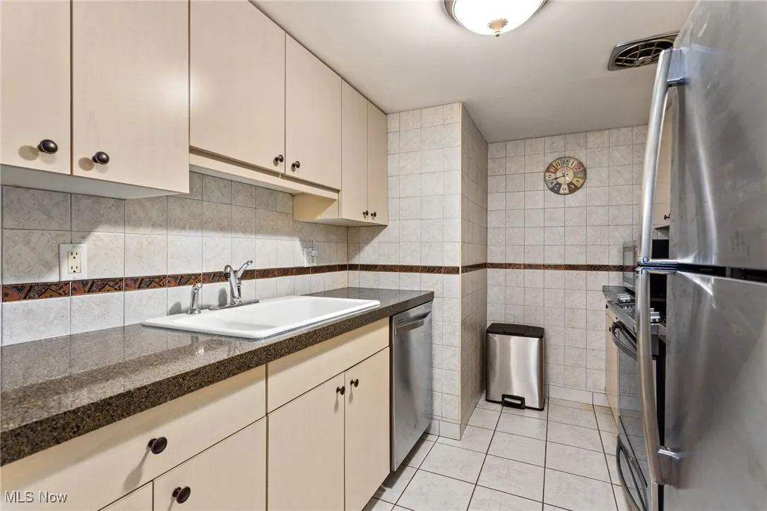 Kitchen with tile walls, dark countertops, stainless steel appliances, light tile patterned floors, and decorative backsplash