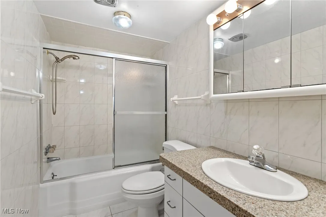 Full bathroom with tile walls, combined bath / shower with glass door, vanity, tile patterned flooring, and backsplash