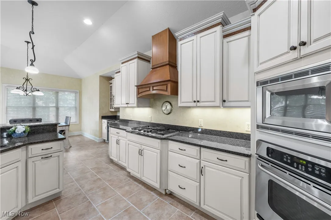 Kitchen featuring stainless steel appliances, pendant lighting, dark stone countertops, white cabinetry, and lofted ceiling
