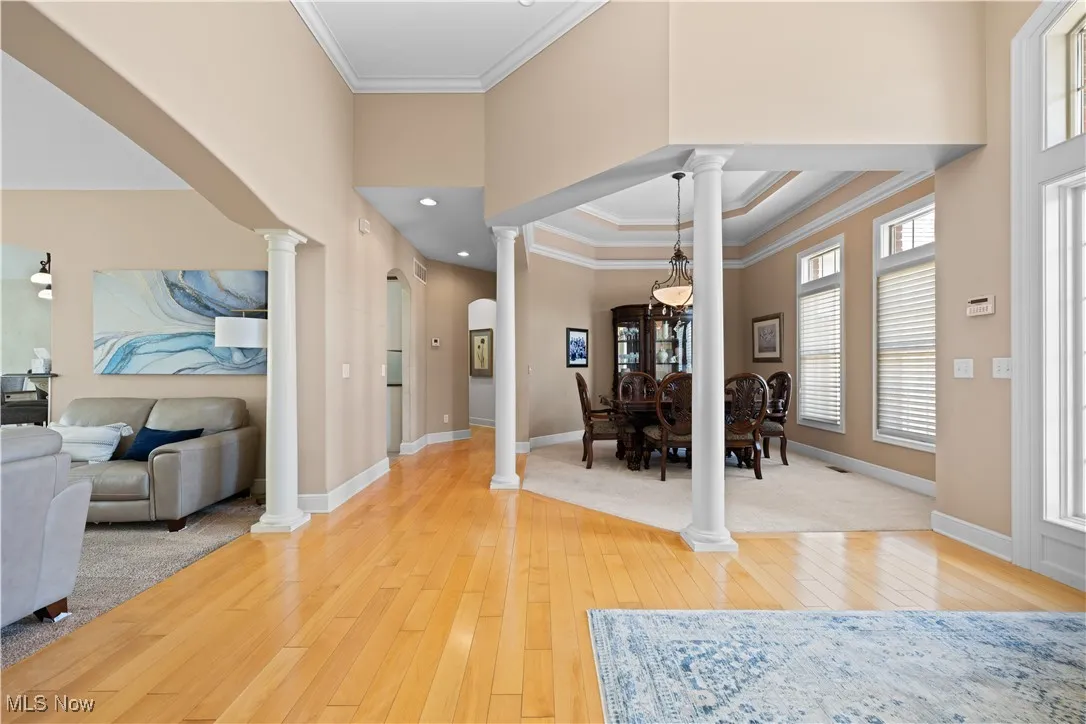 Foyer entrance with ornamental molding, a tray ceiling, light wood-type flooring, decorative columns, and recessed lighting