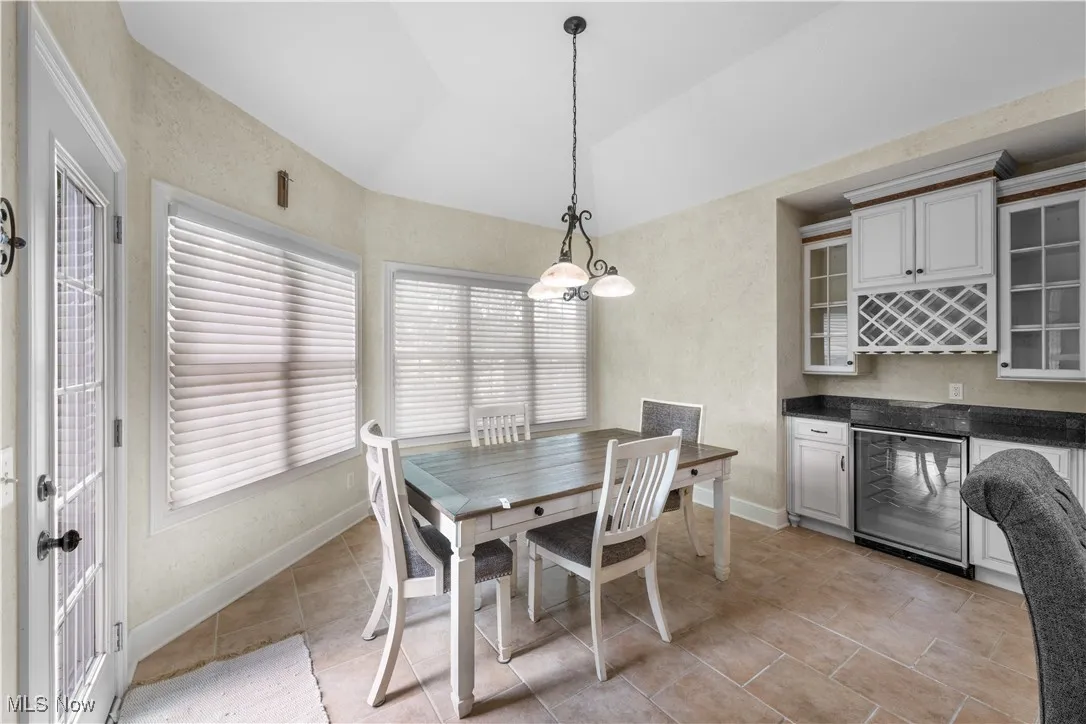 Dining space featuring vaulted ceiling, light tile patterned floors, beverage cooler, and a textured wall