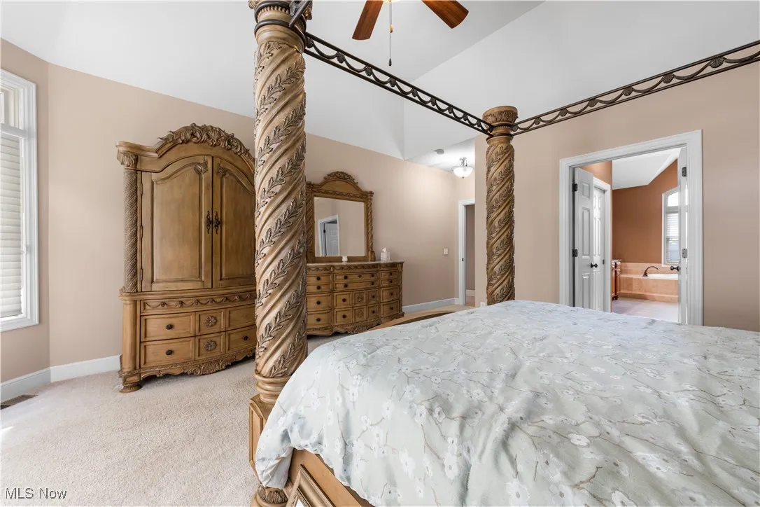 Bedroom with light colored carpet, a ceiling fan, connected bathroom, and a high ceiling