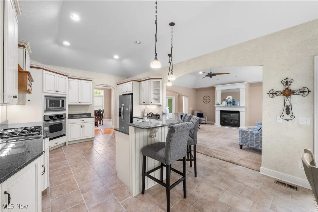 Kitchen featuring arched walkways, a kitchen bar, a glass covered fireplace, decorative light fixtures, and dark stone countertops