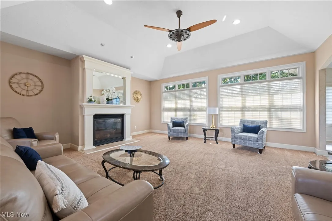 Living area with light colored carpet, a glass covered fireplace, ceiling fan, recessed lighting, and a raised ceiling