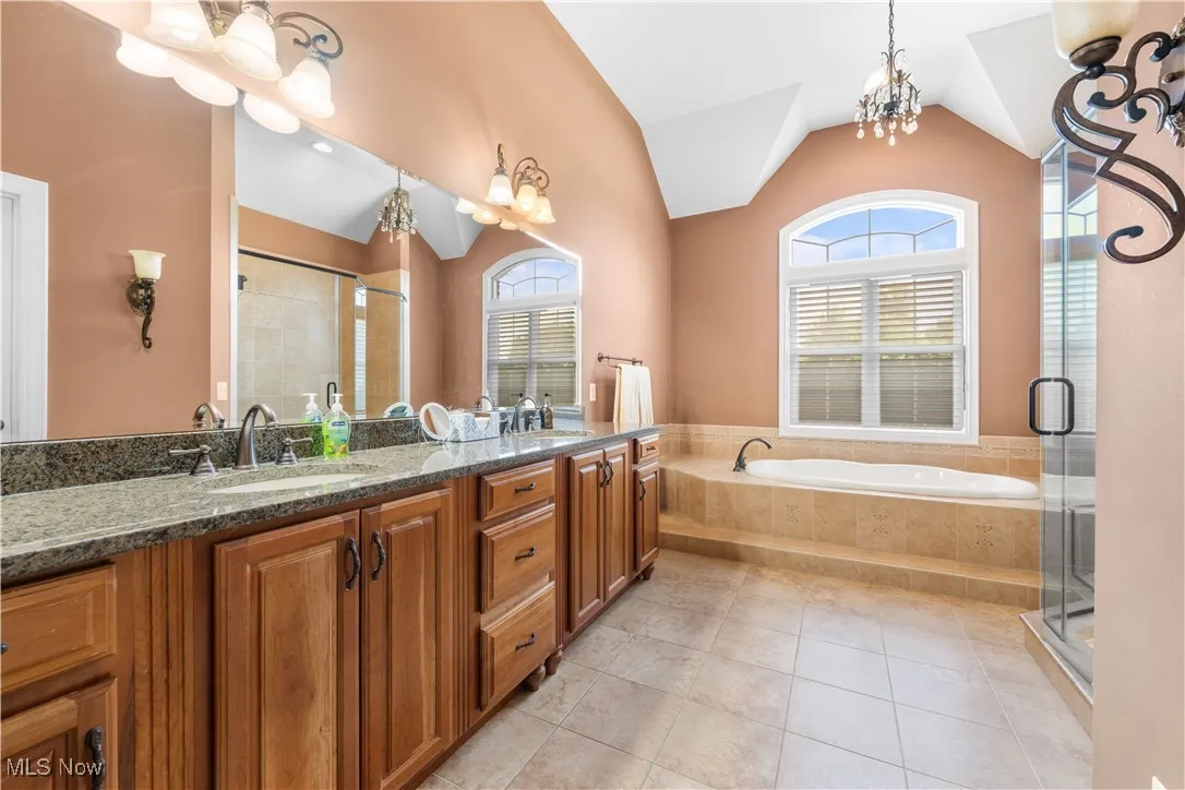 Bathroom featuring a garden tub, double vanity, a chandelier, a stall shower, and light tile patterned floors