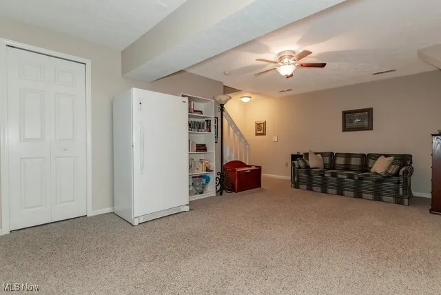 Lower level recreation room with light colored carpet, and ceiling fan