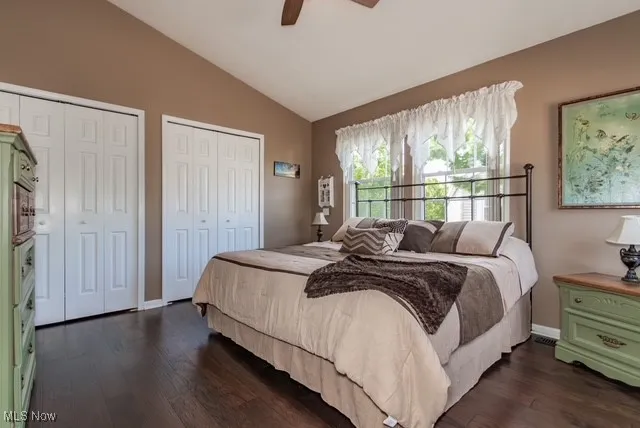 Bedroom with lofted ceiling, multiple closets, dark wood-style flooring, and a ceiling fan