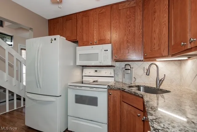 Kitchen with brown cabinets, white appliances, tasteful backsplash, dark stone countertops, and dark wood-type flooring