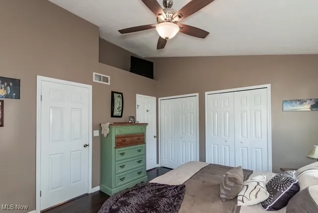 Bedroom featuring multiple closets, dark wood-type flooring, lofted ceiling, and ceiling fan
