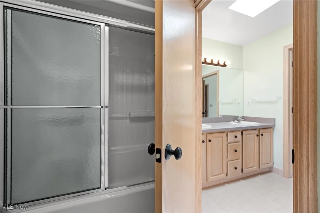 Bathroom with bath / shower combo with glass door, light tile patterned flooring, and a skylight