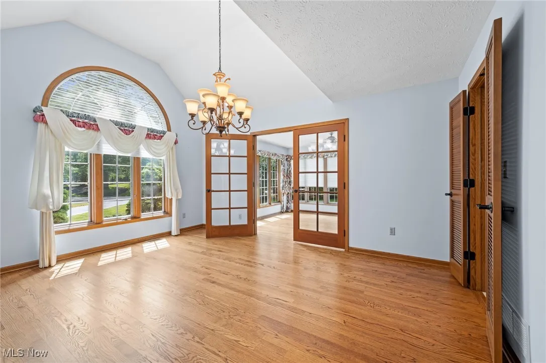 Unfurnished dining room featuring a chandelier, light wood finished floors, french doors, and lofted ceiling