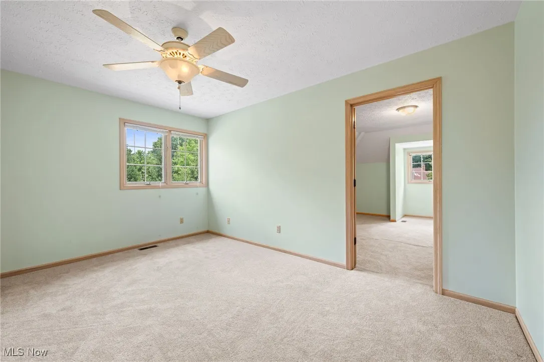 Empty bedroom featuring a textured ceiling, carpet, and a ceiling fan