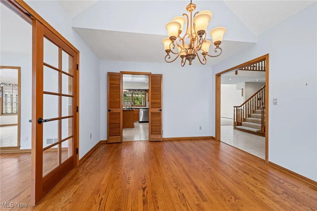 Empty dining room featuring wood-style flooring, a chandelier, and vaulted ceiling