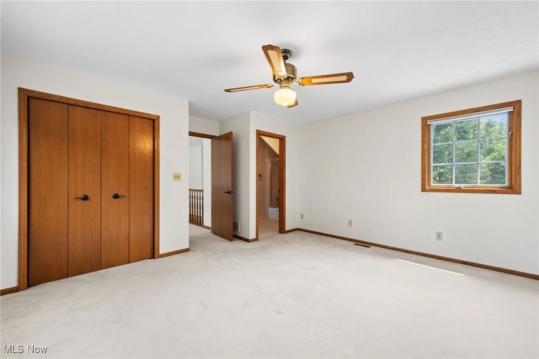 Second floor primary bedroom with ceiling fan, a closet, ensuite bath, and light carpet