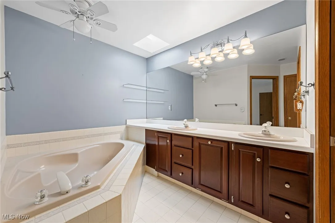 First floor primary bathroom featuring a skylight, ceiling fan, a bath, and light tile patterned floors