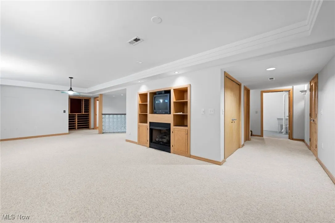 Recreation room featuring light carpet, recessed lighting, built in shelves, a fireplace, and ornamental molding