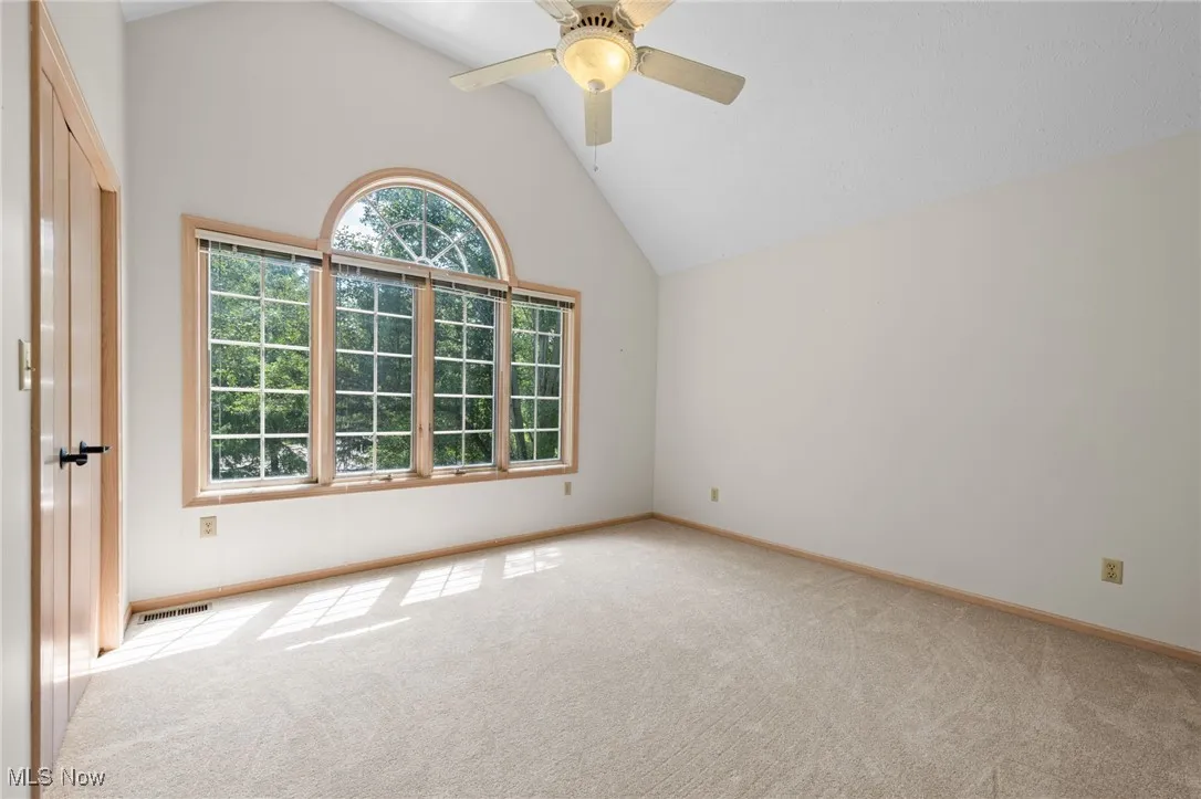 Empty room featuring light colored carpet, ceiling fan, and high vaulted ceiling