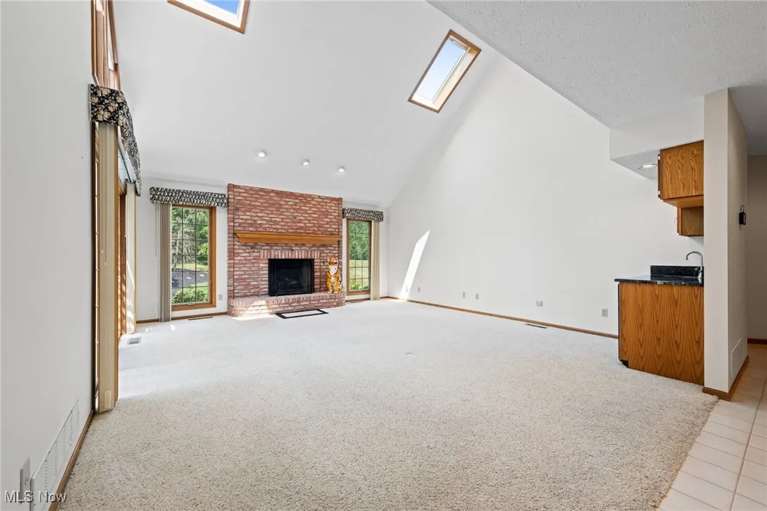 Unfurnished living room featuring a skylight, light colored carpet, high vaulted ceiling, a brick fireplace, and a textured ceiling