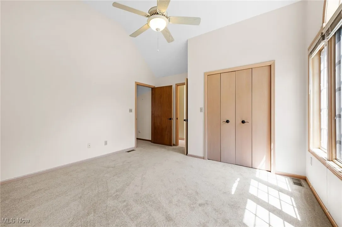 Unfurnished bedroom featuring light carpet, a closet, high vaulted ceiling, and ceiling fan