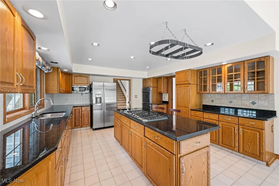 Kitchen with tasteful backsplash, dark stone counters, appliances with stainless steel finishes, brown cabinets, and recessed lighting