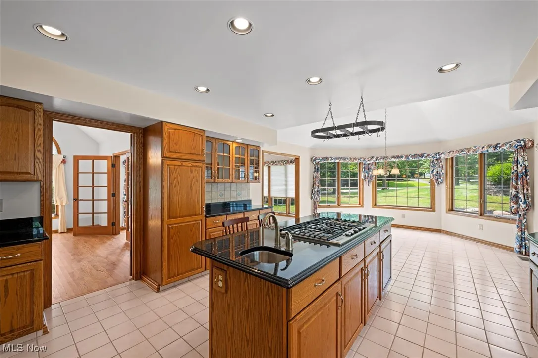 Kitchen with brown cabinetry, light tile patterned floors, recessed lighting, plenty of natural light, and a kitchen island with sink