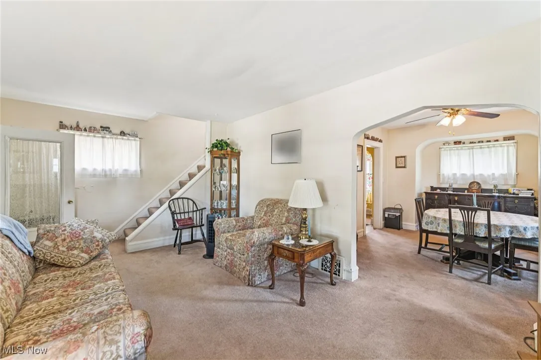 Living area with stairway, carpet floors, ceiling fan, and arched walkways