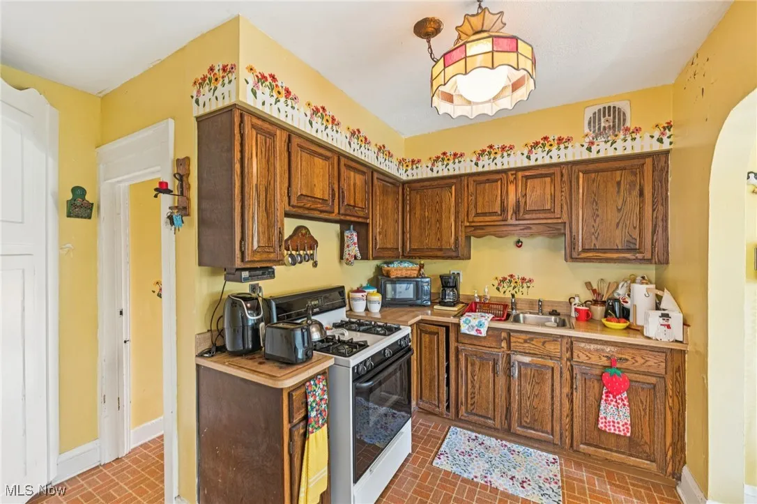 Kitchen featuring white range with gas cooktop, brick patterned floors, and black microwave