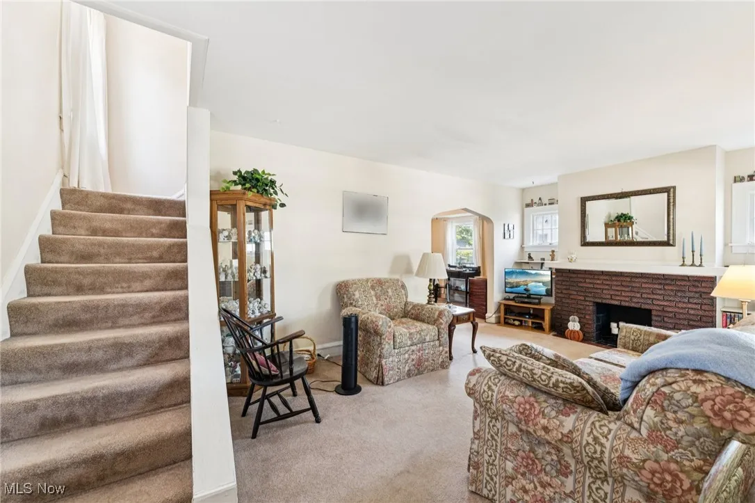 Carpeted living area featuring a brick fireplace, arched walkways, and stairway