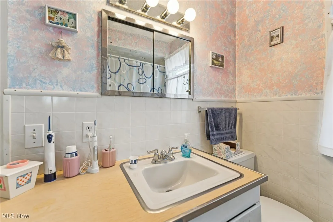 Bathroom with wallpapered walls, vanity, wainscoting, a shower with curtain, and tile walls