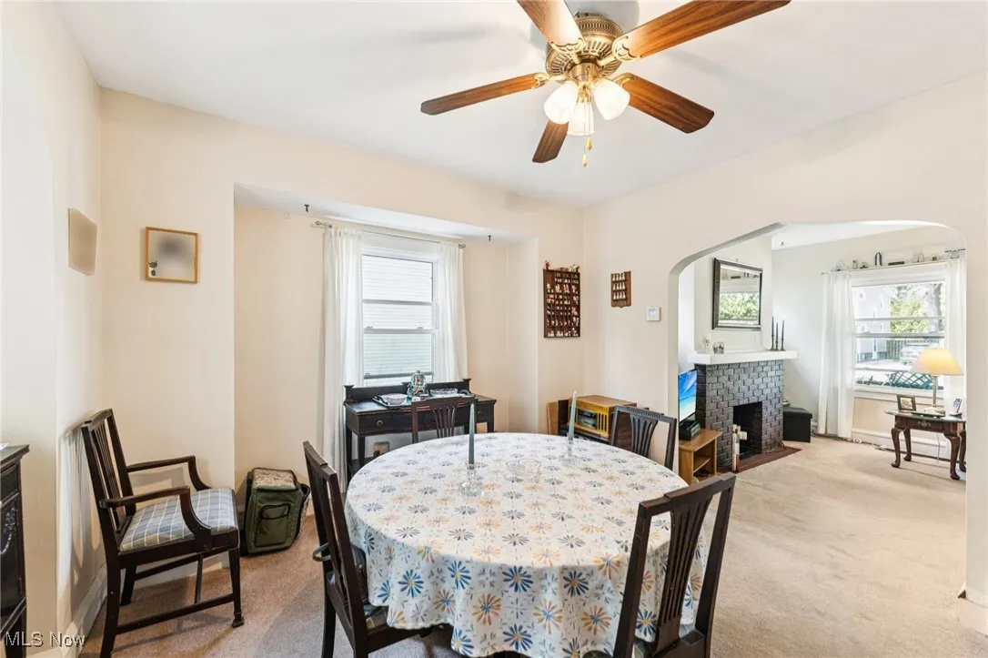 Dining space with arched walkways, light carpet, a fireplace, and ceiling fan