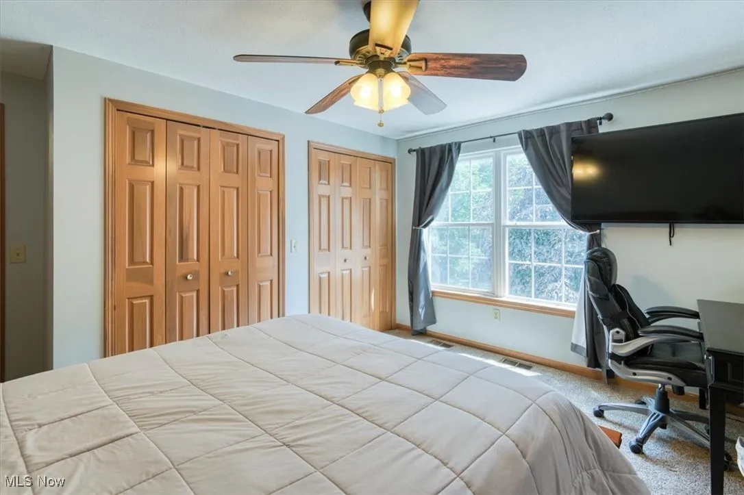 Carpeted bedroom featuring two closets, ceiling fan, and an office area