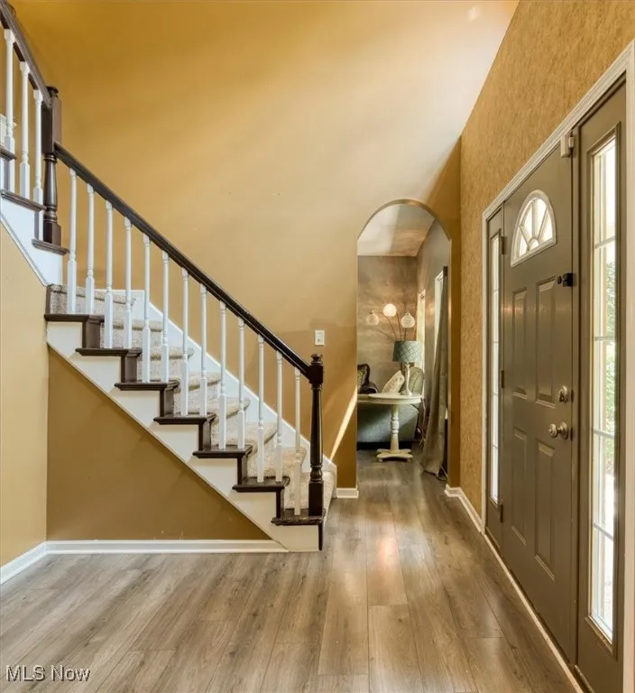 Foyer featuring stairs, arched walkways, light wood-type flooring, and plenty of natural light
